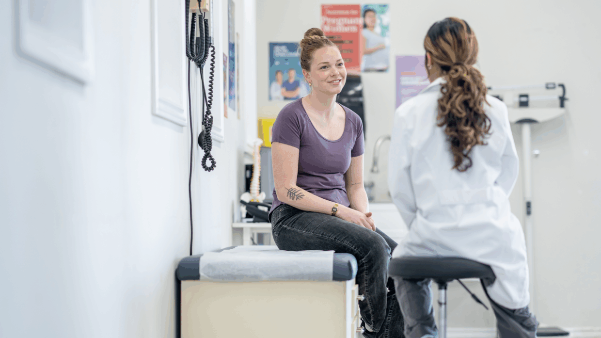 woman sitting on an exam table speaking to a woman doctor