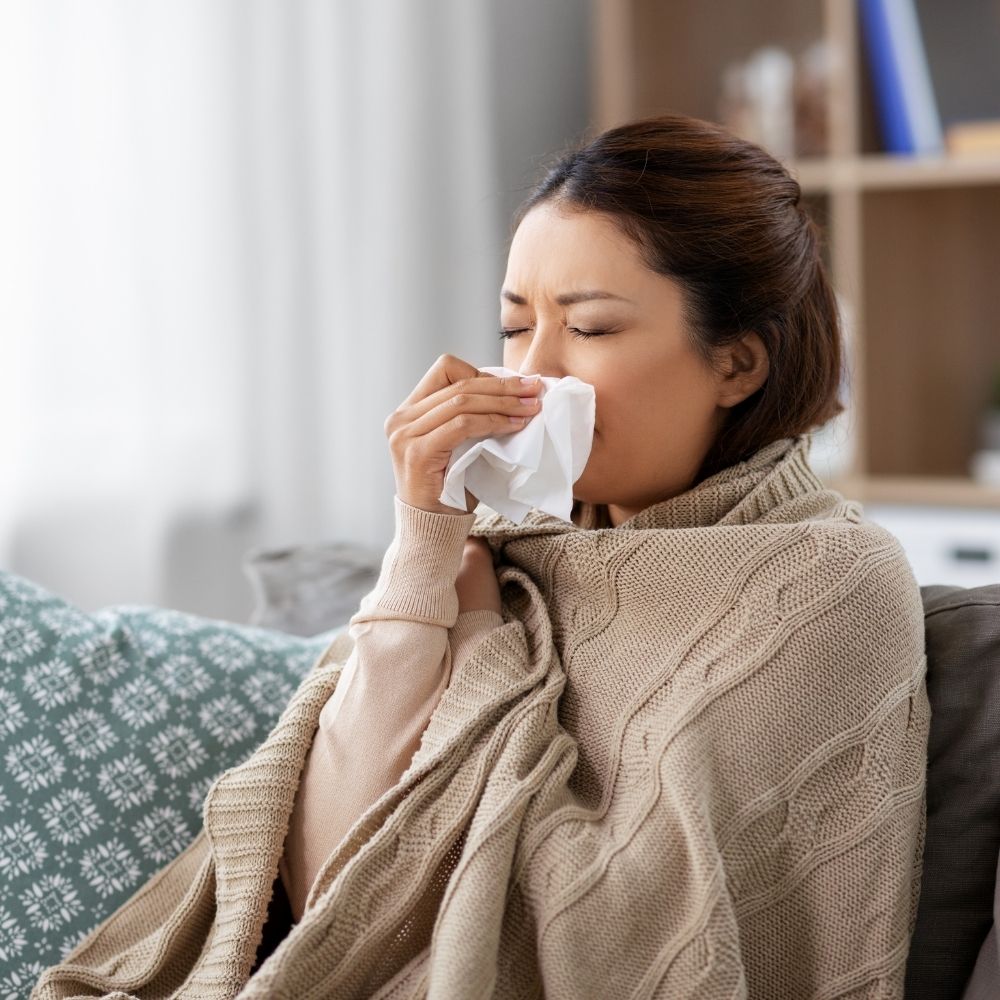 woman sitting on couch with tissue and blanket ill with the flu