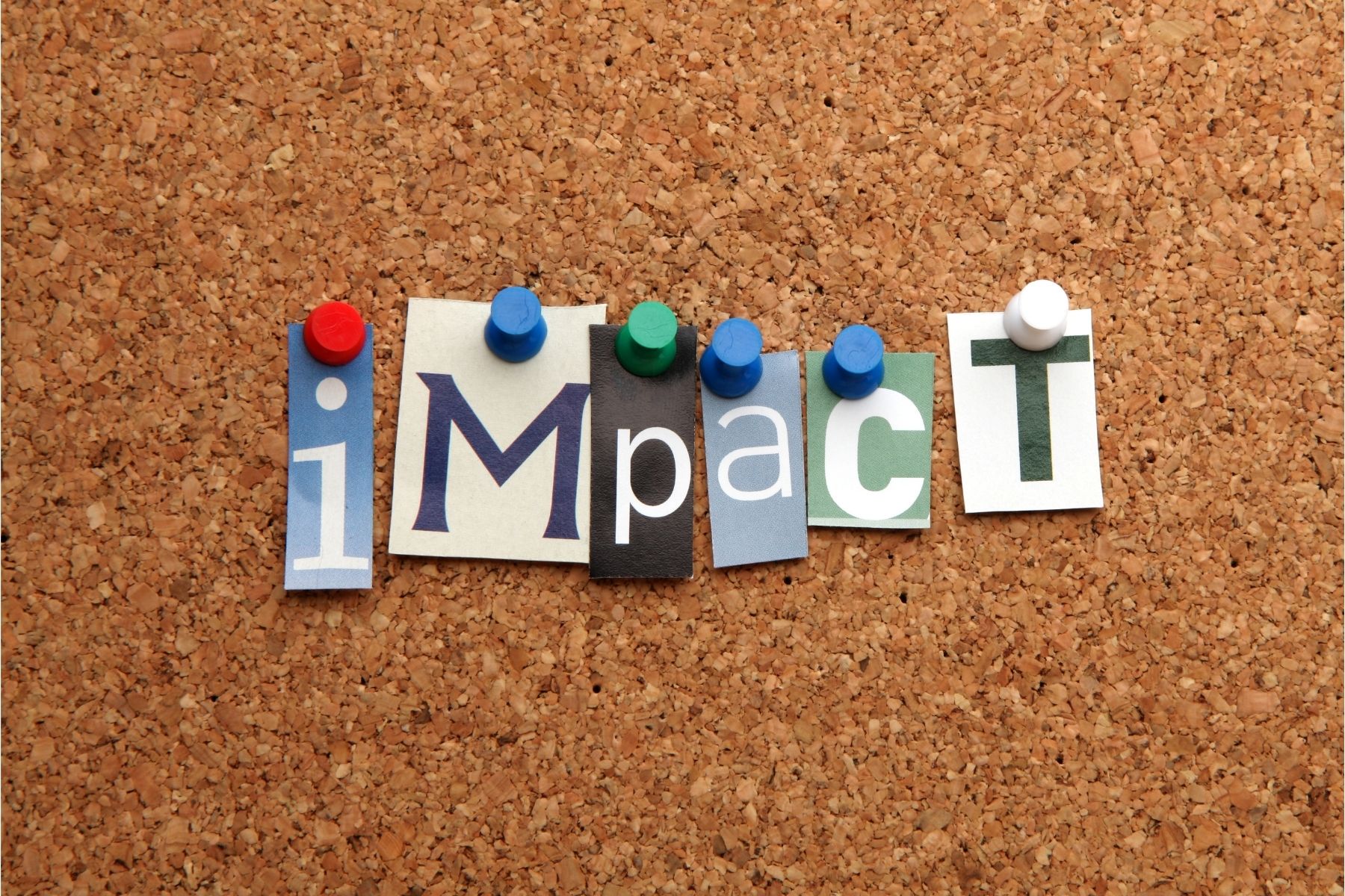 The letters spelling Impact pinned on a cork board.